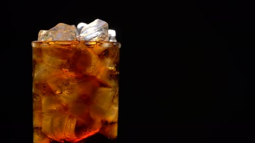 Cola mit Eis und Blasen im Glas rotierend auf Schwarz