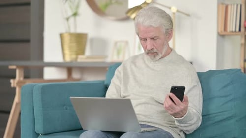 Senior Man Using Laptop and Smartphone at Home