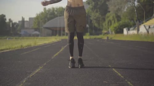 Front View of Young Caucasian Sportsman Jumping Rope on Athletic Field. Portrait of Concentrated Man