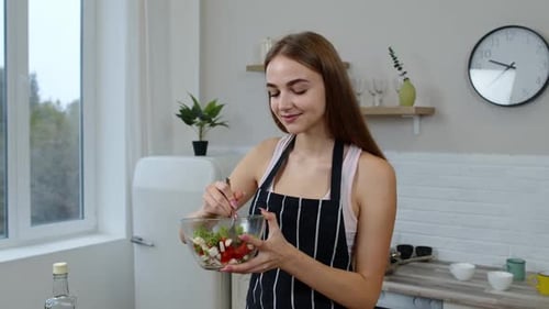 Woman Preparing and Tasting Fresh Salad in Kitchen