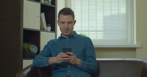 Man Uses Smartphone Sitting on Couch Indoors