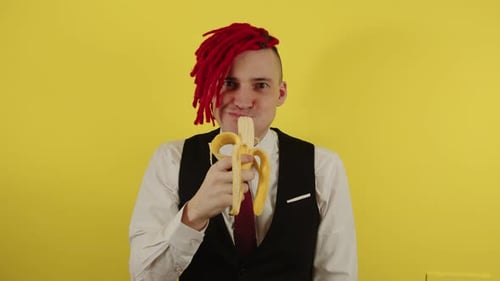 Young Man in White Shirt Vest and Tie Greedily Eating Banana on Yellow Background in Studio
