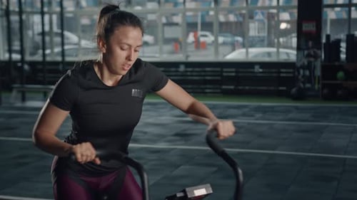 Young female athlete trains cardio on a bicycle with a fan, cardio and endurance training