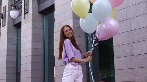 Romantic Smiling Red-haired Girl Standing with Large Fountain of Colorful Balloons Outside.