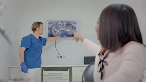 Male Dentist In Dental Office Shows Patient Image Of Her Teeth On Big Screen