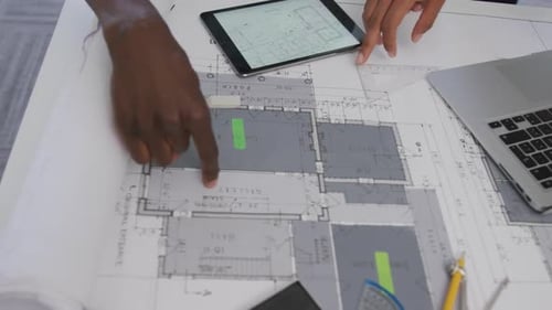 Hands of biracial male and female architects using tablet and checking architects plans in office