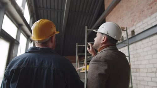 Two Men in Hard Hats Inspect Building Under Construction