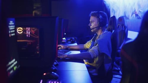 Guy Is Sitting in a Computer Club, Playing an Online Game. Company of Young People Sits in a