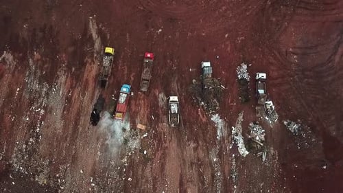 Straight down aerial view of dump trucks unloading garbage at a landfill