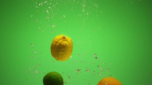 Citrus Fruits Falling in Water with Bubbles Green Background in Slow Motion Orange Lime Lemon