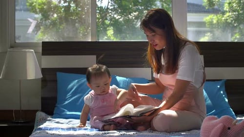 Mother Reading to Baby on Bed at Home