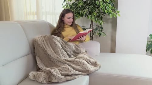 Woman Reading Book on Couch Indoors with Blanket
