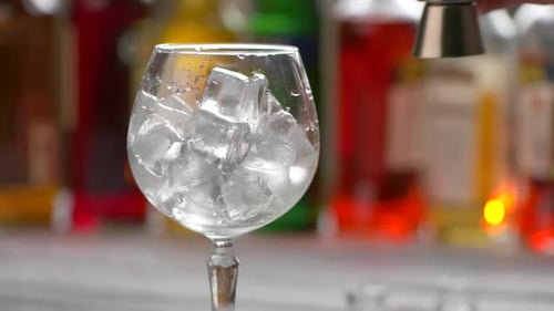 Ice and Water in Glass with Colorful Bottles