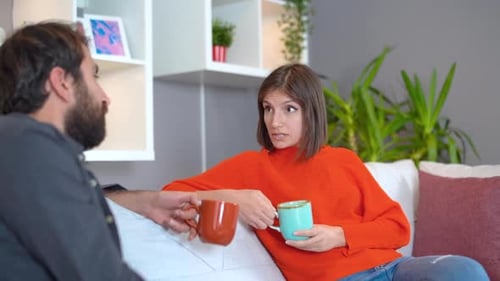 Woman Talking to Man on Couch Holding Mugs