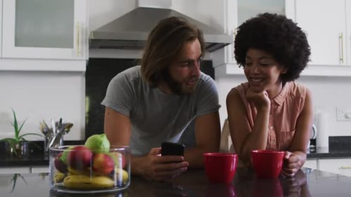 Woman and Man Looking at Cellphone in Kitchen
