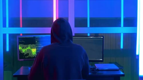 Rückansicht von Hacker in einer schwarzen Jacke und einer Kapuze auf dem Kopf, der Hacker-Programme schreibt