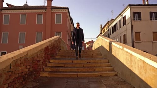 Man Walks Along Ancient Bridge with Stone Steps and Arch