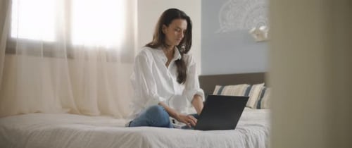 Woman working on laptop sitting on bed