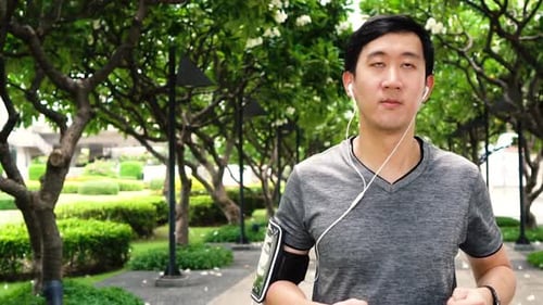 Slow Motion Video of Young Asian Man Jogging While Listening to Music at Park