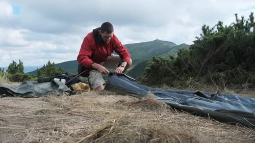 Man Setting Up a Camping Tent in Mountains