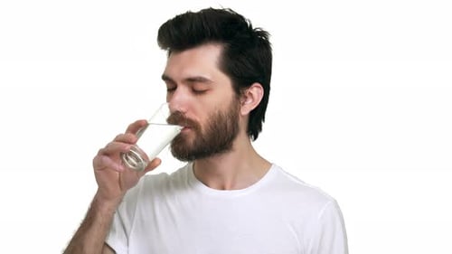 Kaukasischer Mann hält ein Glas Wasser und trinkt lächelnd zufrieden auf weißem Hintergrund