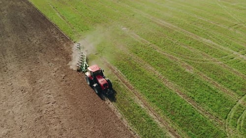 Farmer on a Red Tractor Plows the Dusty Arid Soil