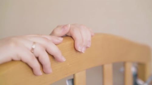 Careful Mother Hands Rock Wooden Crib in Light Room Closeup