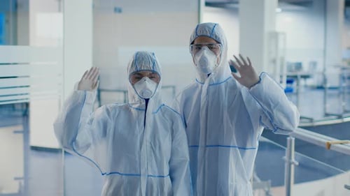 Two Workers in Protective Gear Waving at Camera