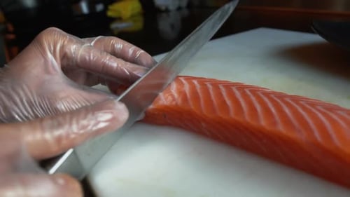 Gloved Hands Cutting Fresh Salmon With Sharp Knife