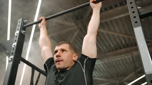 Portrait of a Strong Athlete Pulling Up on the Horizontal Bar in the Gym