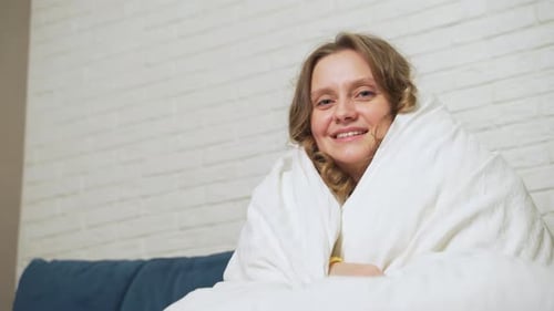 Mujer envuelta en manta blanca sentada y sonriendo