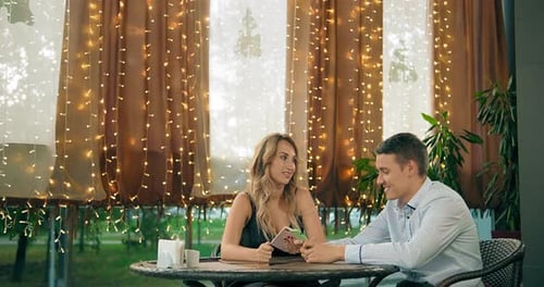 Man and Girlfriend Look at Photos on Smartphone in Cafe