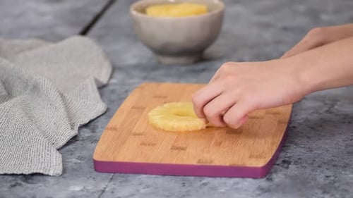 Hands Slicing Pineapple on Cutting Board