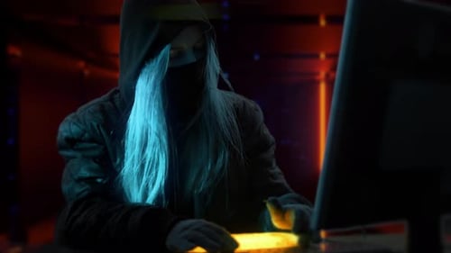 Hooded Figure Works at Computer in Dark Room