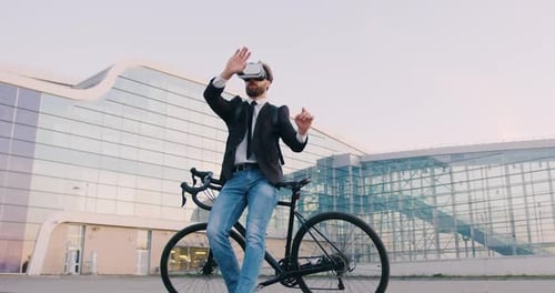 Homme d'affaires en casque de réalité virtuelle debout près de son vélo et travaillant sur un écran imaginaire