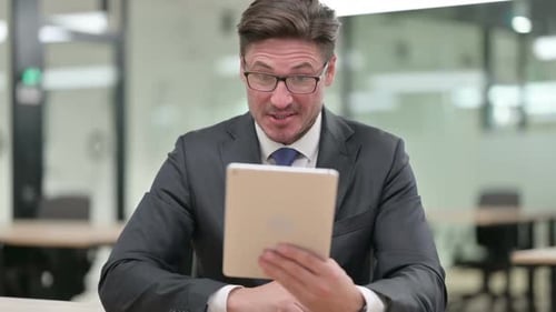 Executive Man Enjoys Tablet Video Call in Office