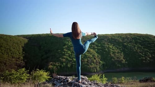 Woman in Blue Overalls Practicing Yoga Utthita Hasta Padangushthasana on High Cliff Above Water
