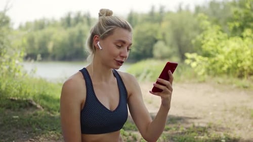 Young Woman Uses Smartphone and Drinks Water Outdoors