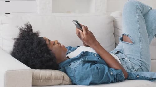 Woman Laughing While Using Phone On Sofa