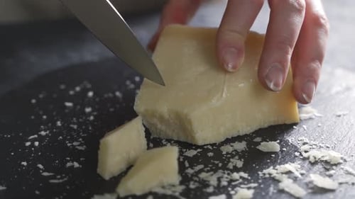 Composition of Italian Cheese, on a Black Cutting Board. One Hand Takes the Knife and Breaks a
