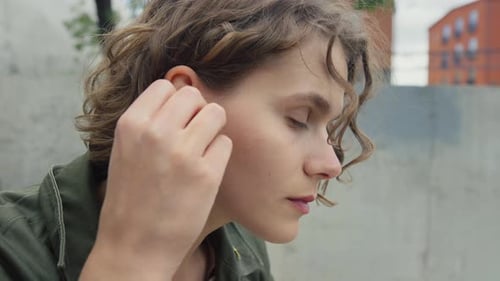 Woman Uses Phone and Earbuds in Urban Setting