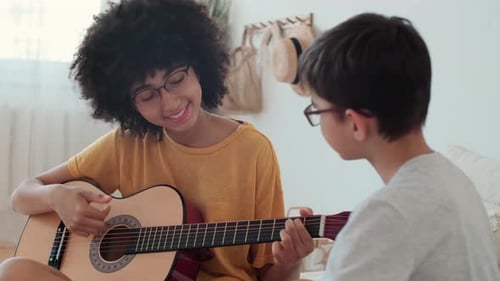 Teen Girl Plays Guitar for Young Boy Indoors
