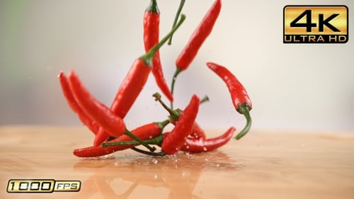 Red chili peppers falling onto wet wooden surface