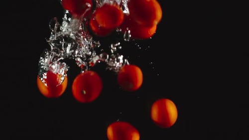 Tomates cerises tombent sous l'eau sur fond noir