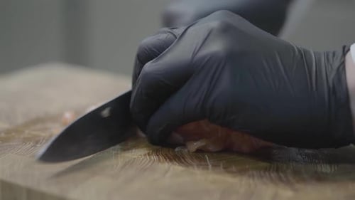 Hands of Chef in Restaurant Uniform and Black Gloves Cutting Slices of Tuna Fish