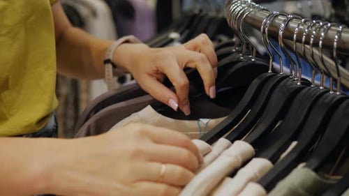 A Woman in a Clothing Store Looks at Tshirts or Blouses Hung on Hangers