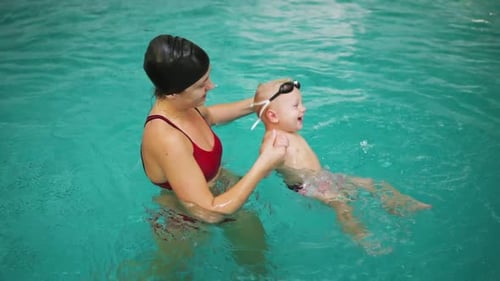 Junge Mutter bringt ihrem kleinen Jungen das Schwimmen im Schwimmbad bei