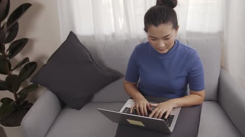 Woman Working on Laptop Computer from Gray Couch