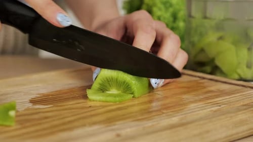 Woman Slices Fresh Kiwi on Wooden Board