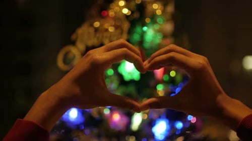 Hands Make Heart in front of Christmas Tree